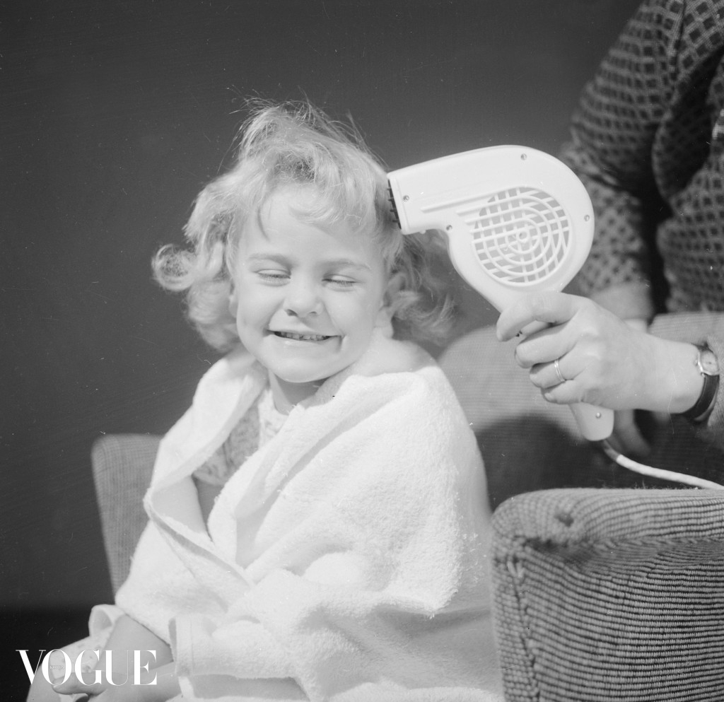 29th October 1959:  Wrapped in a towel, a little girl is having her hair dried with a hand held hair dryer.  Mother - pub. 1959  (Photo by Chaloner Woods/Getty Images)