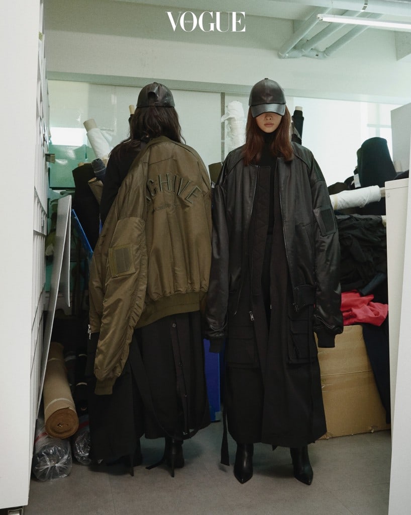 준지의 아이코닉한 오버사이즈 트렌치 코트와 MA-1 재킷을 입고 준지 사무실의 원단 더미 앞에서 포즈를 취했다. 의상과 액세서리는 2017 F/W 컬렉션.